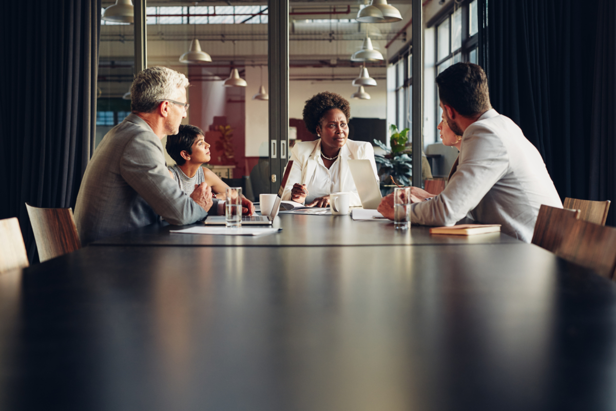 Diverse businesspeople sitting around a boardroom table discussing work ...